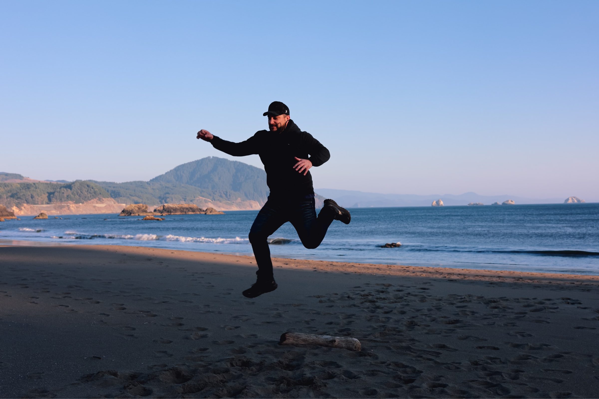 Joshua Brown jumping mid-air on a beach on the Oregon coast.