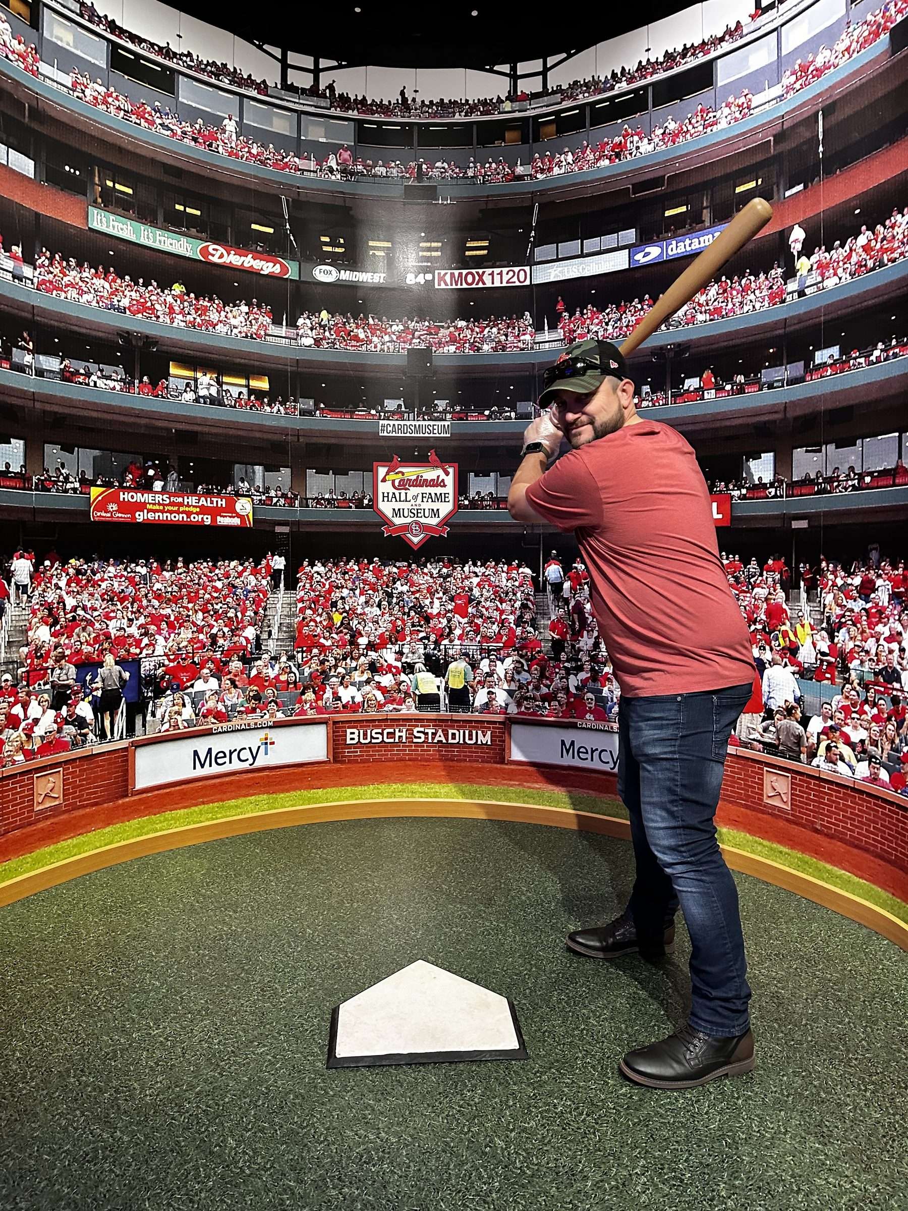 Joshua Brown posing with a bat at home plate in front of a Busch Stadium backdrop at the Cardinals Hall of Fame Museum.