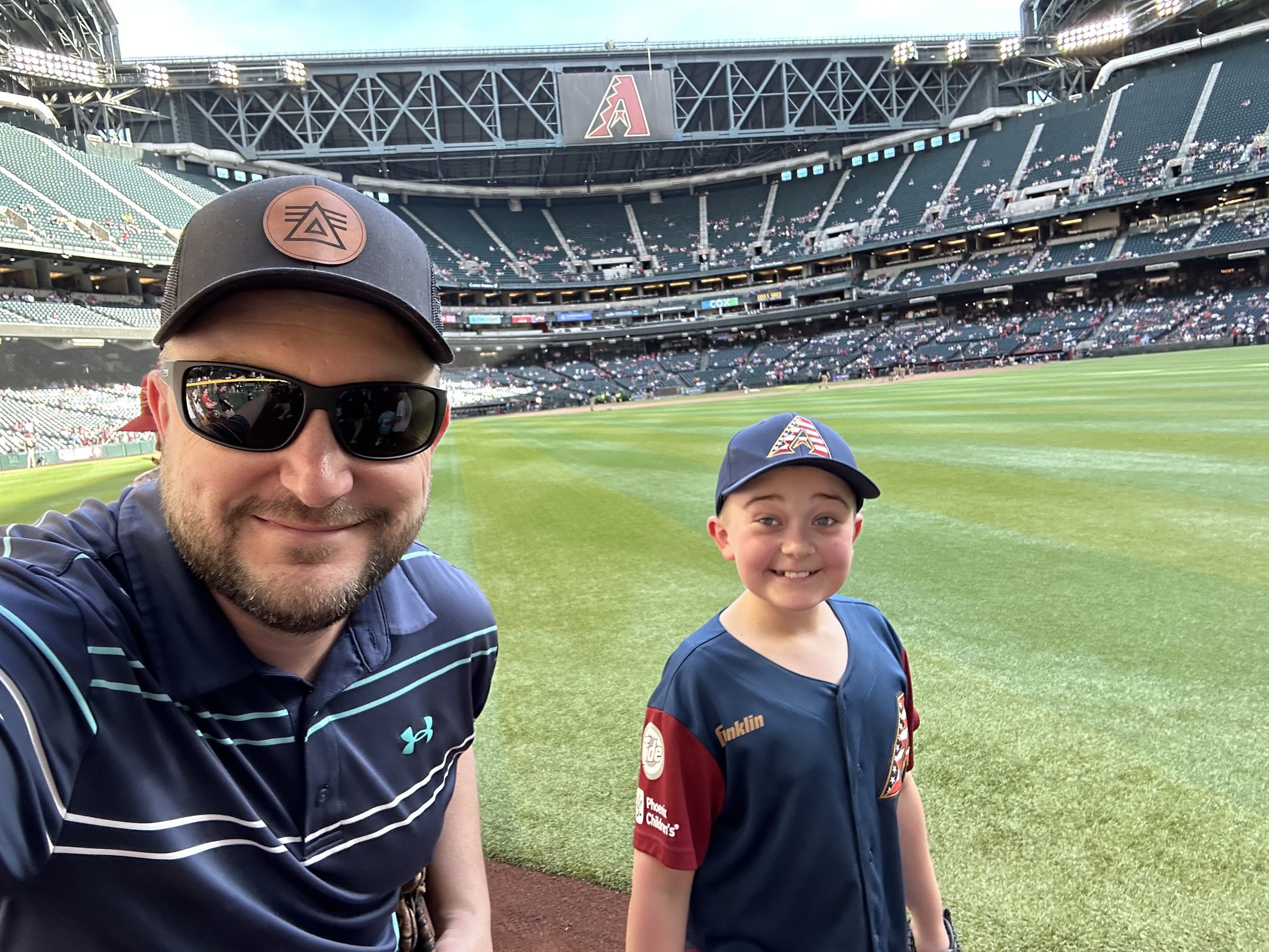 Joshua Brown taking a selfie with his son on the field at a baseball stadium.