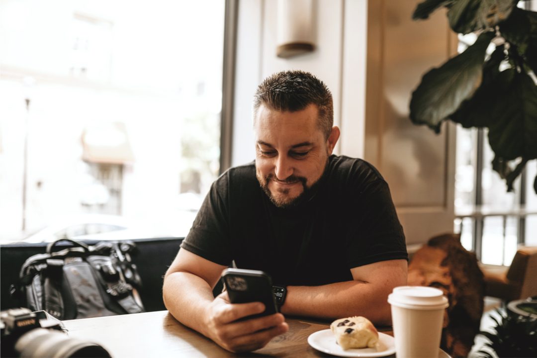 Joshua Brown smiling at his phone at a table in a Portland coffee shop.