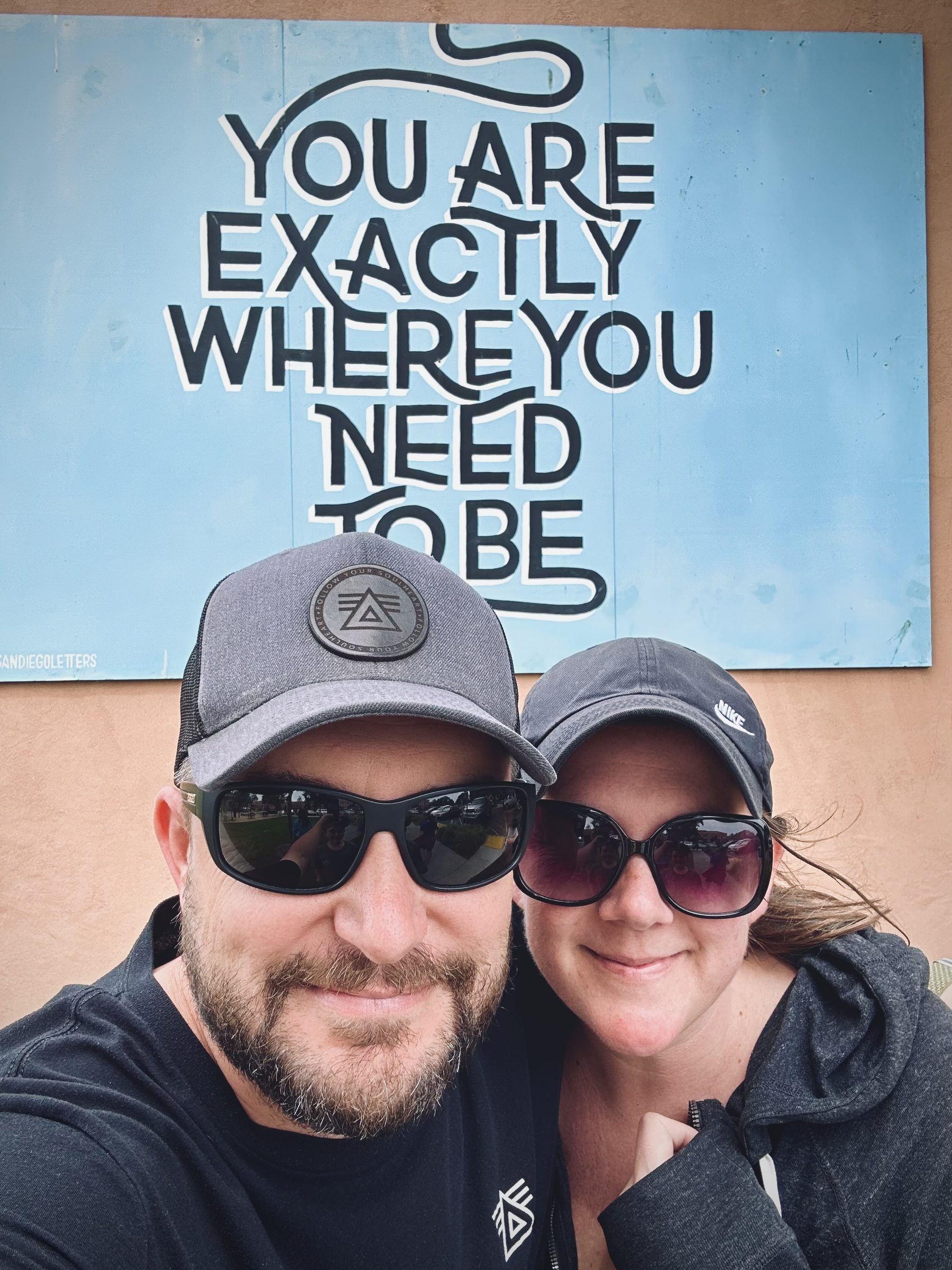 Joshua Brown and Laura taking a selfie in front of a mural that reads, You are exactly where you need to be.