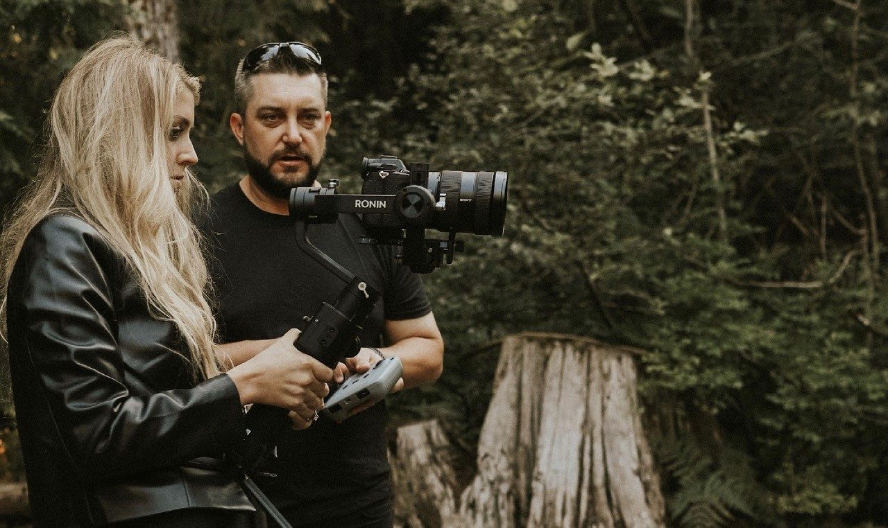 Joshua Brown holding a cinema camera on a gimbal in a forest with a colleague.