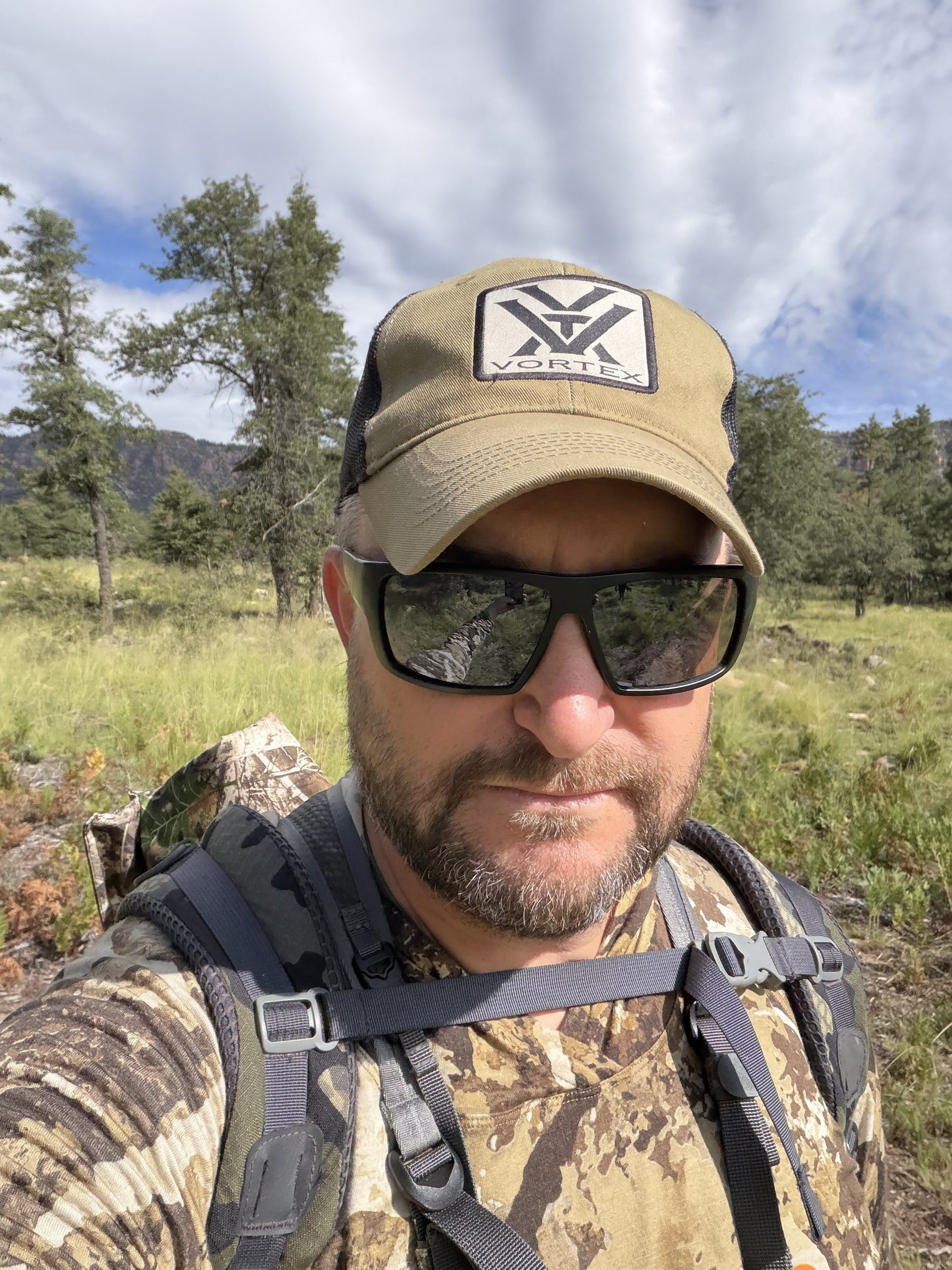 Joshua Brown in camouflage and a hunting pack standing among pine trees.