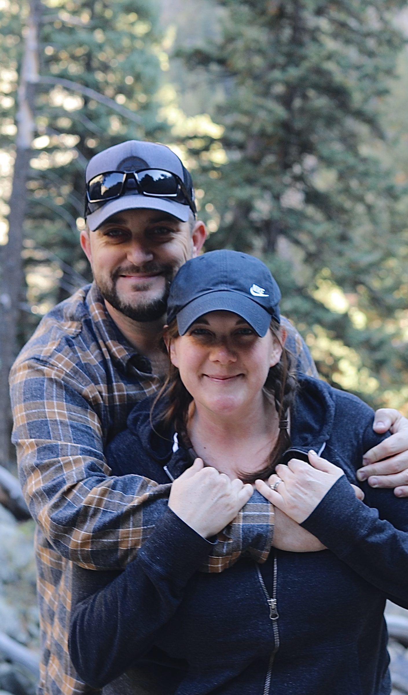 Joshua Brown hugging his wife, Laura, from behind among pine trees.