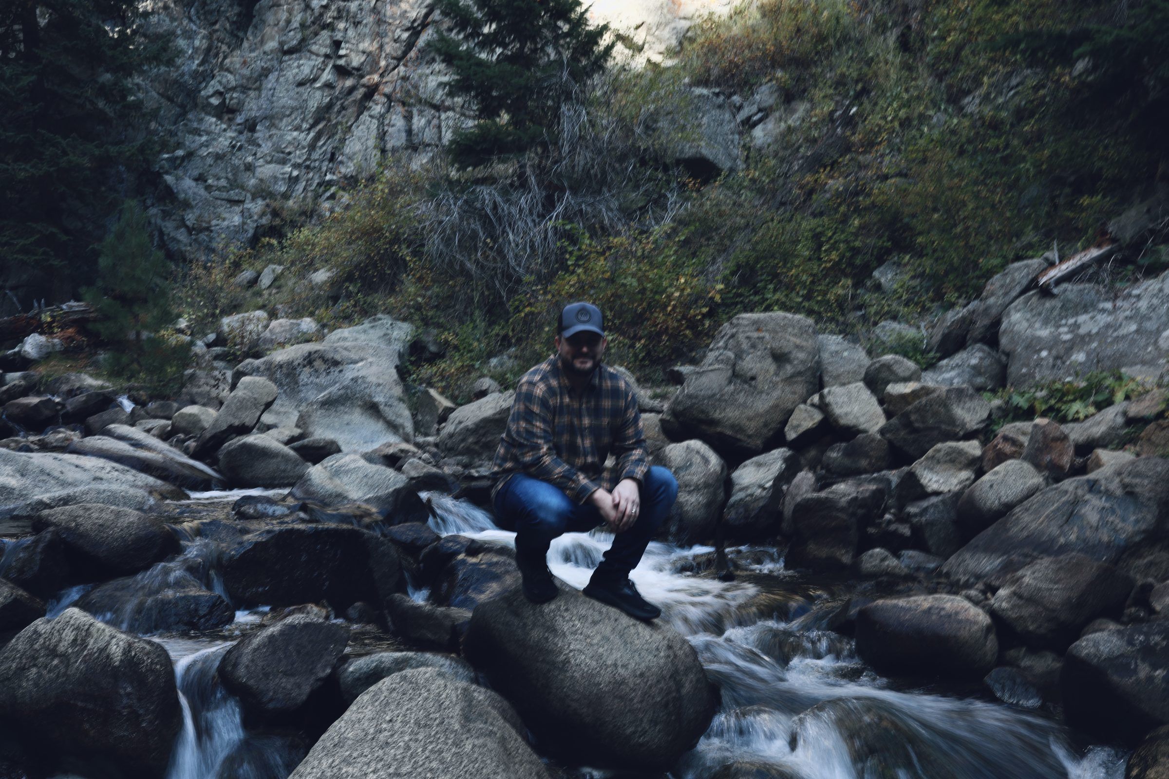 Joshua Brown crouching on a boulder in a rushing mountain creek.