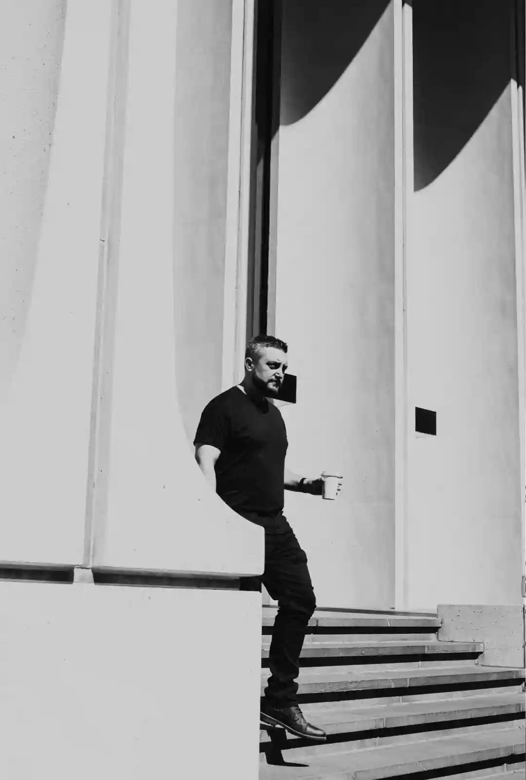 Black and white photo of Joshua Brown walking down concrete stairs holding a coffee.